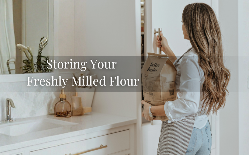 Woman holding a bag of Better Basics Milling organic flour while opening a pantry cabinet in a bright kitchen, demonstrating proper storage of freshly stone-milled flour.